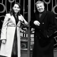 Emilian Kamiński z żoną przed teatrem. Para w eleganckich płaszczach, uśmiechnięci, pozują do zdjęcia.