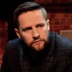 Kamil Maćkowiak w garniturze, z zarostem, w rozmowie.