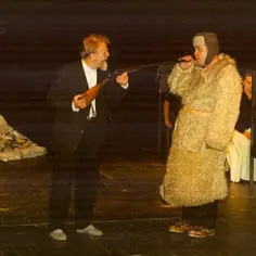 Na scenie, w sztuce inspirowanej Learem, mężczyzna w futrzanym płaszczu i czapce słucha groźby z lufy strzelby, którą trzyma drugi aktor.