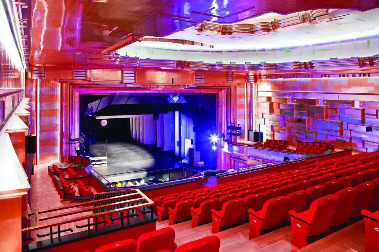 Elegancka scena teatralna z czerwonymi fotelami i mieniącym się sufitem.