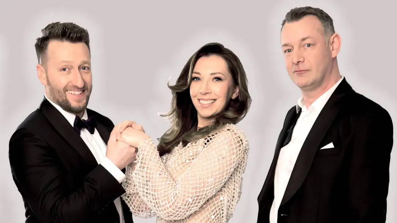 Kabaret Nowaki skład: uśmiechnięty mężczyzna w czarnym smokingu, kobieta w błyszczącej sukience i mężczyzna w czarnym garniturze.